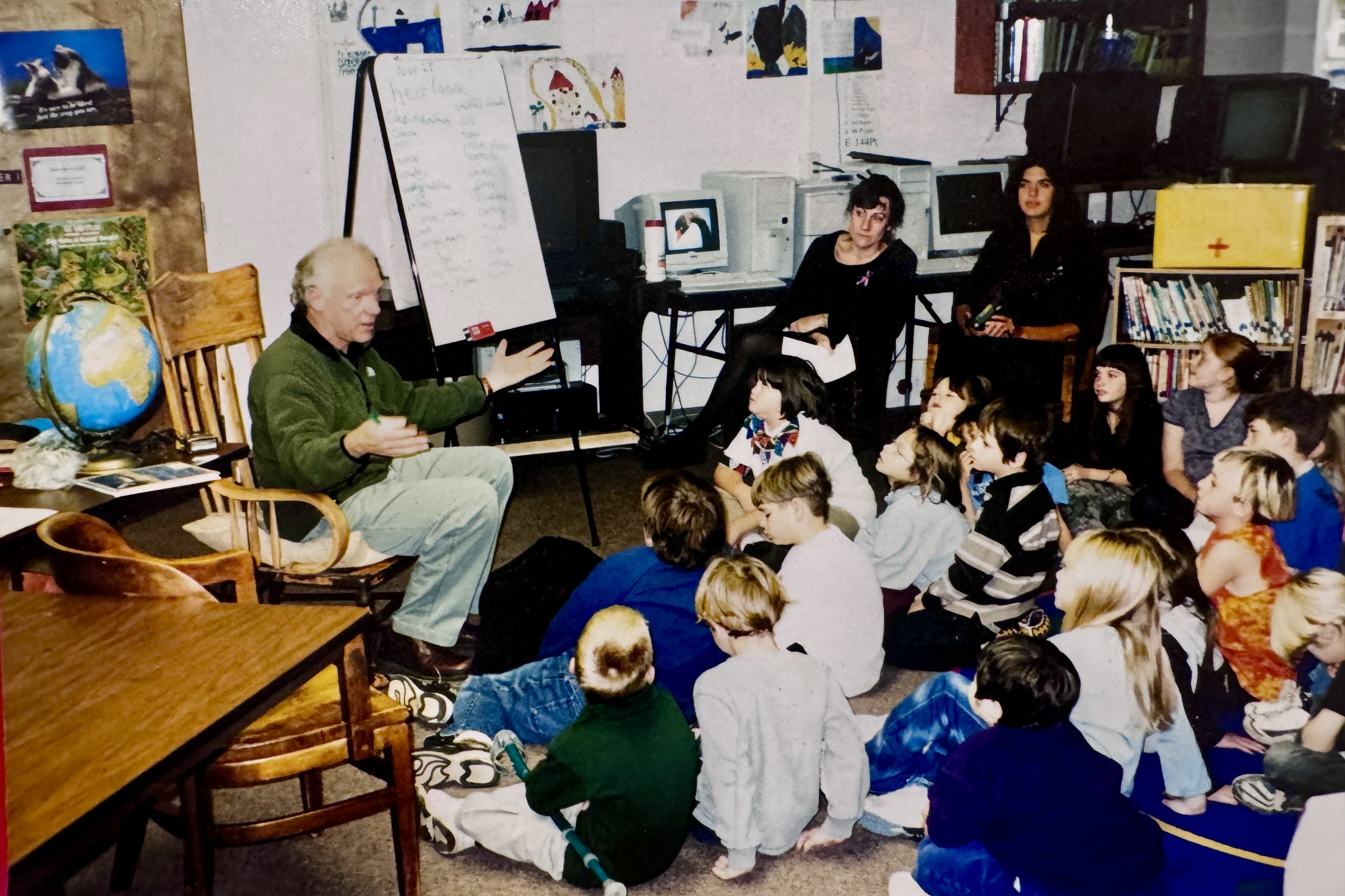 A speaker engages a group of attentive children in a classroom setting.