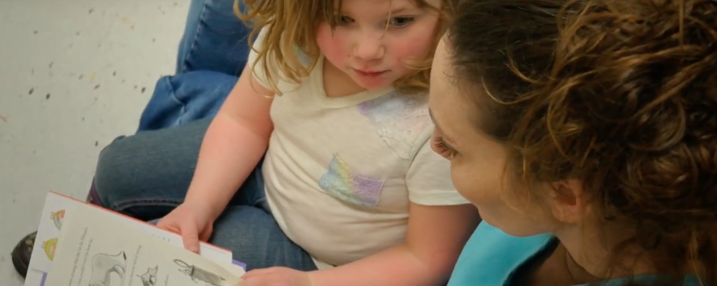 A child and adult read a picture book together, sharing a moment of learning.