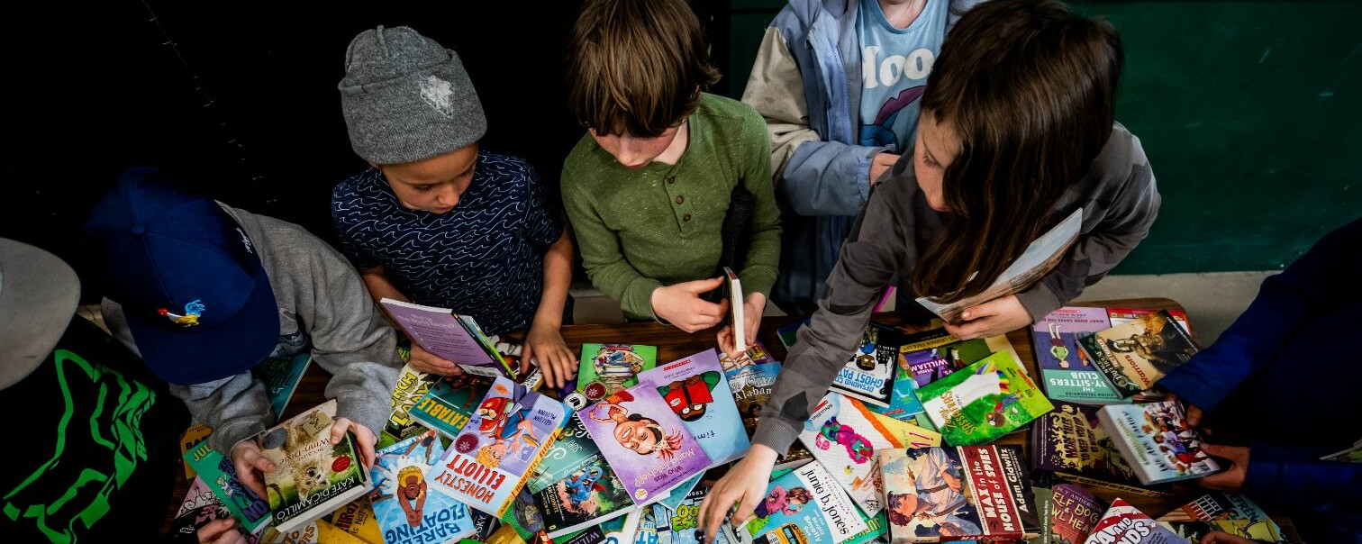 Children exploring a colorful array of books on a table.