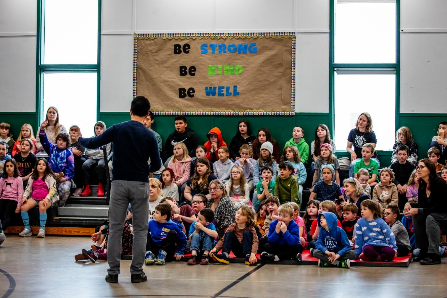 A speaker addresses a large group of attentive children in a school setting.
