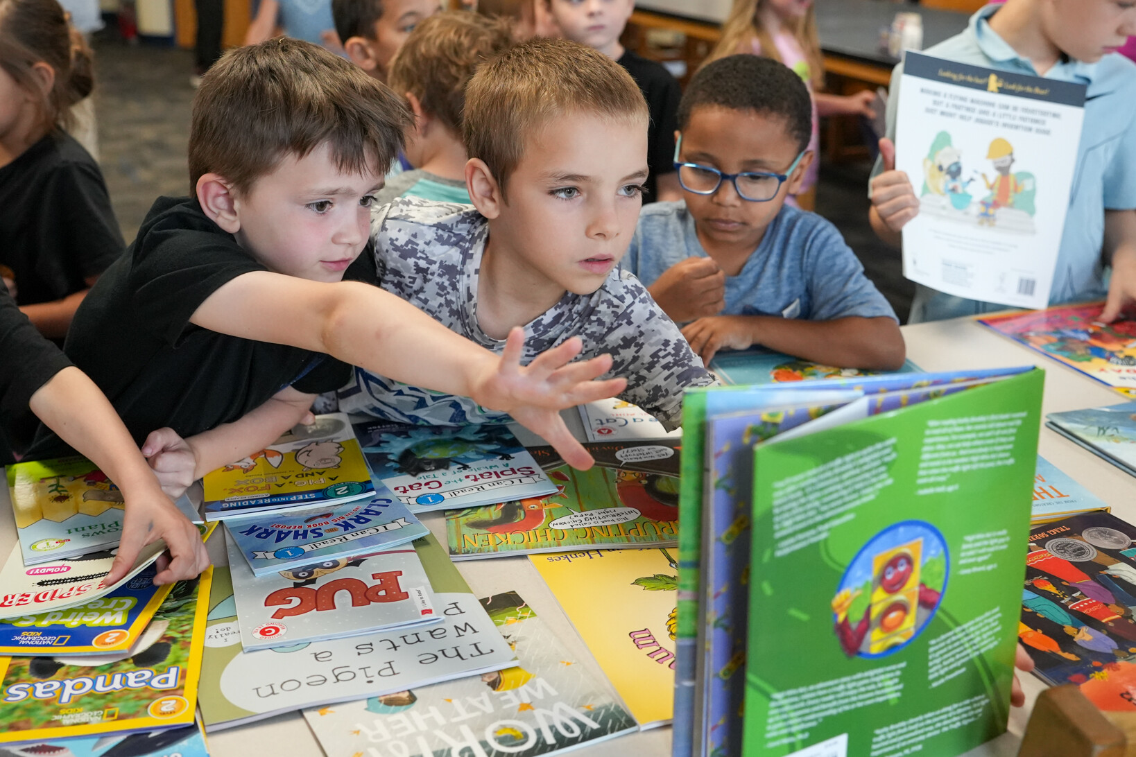 Children eagerly explore a table full of colorful books in a classroom setting.