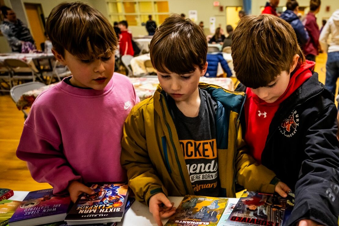 Three children examine comic books at a table in a community space.