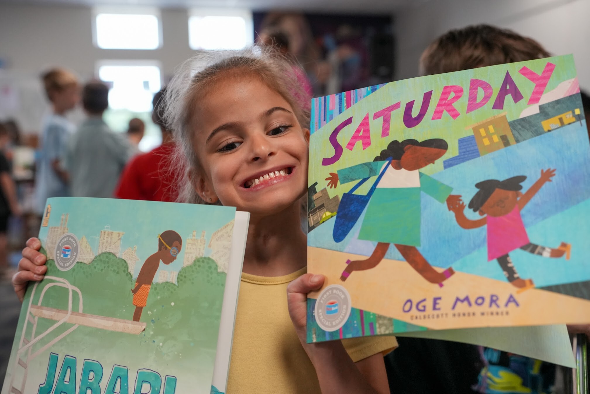Smiling child holding two picture books titled "Saturday" and "Jabari".