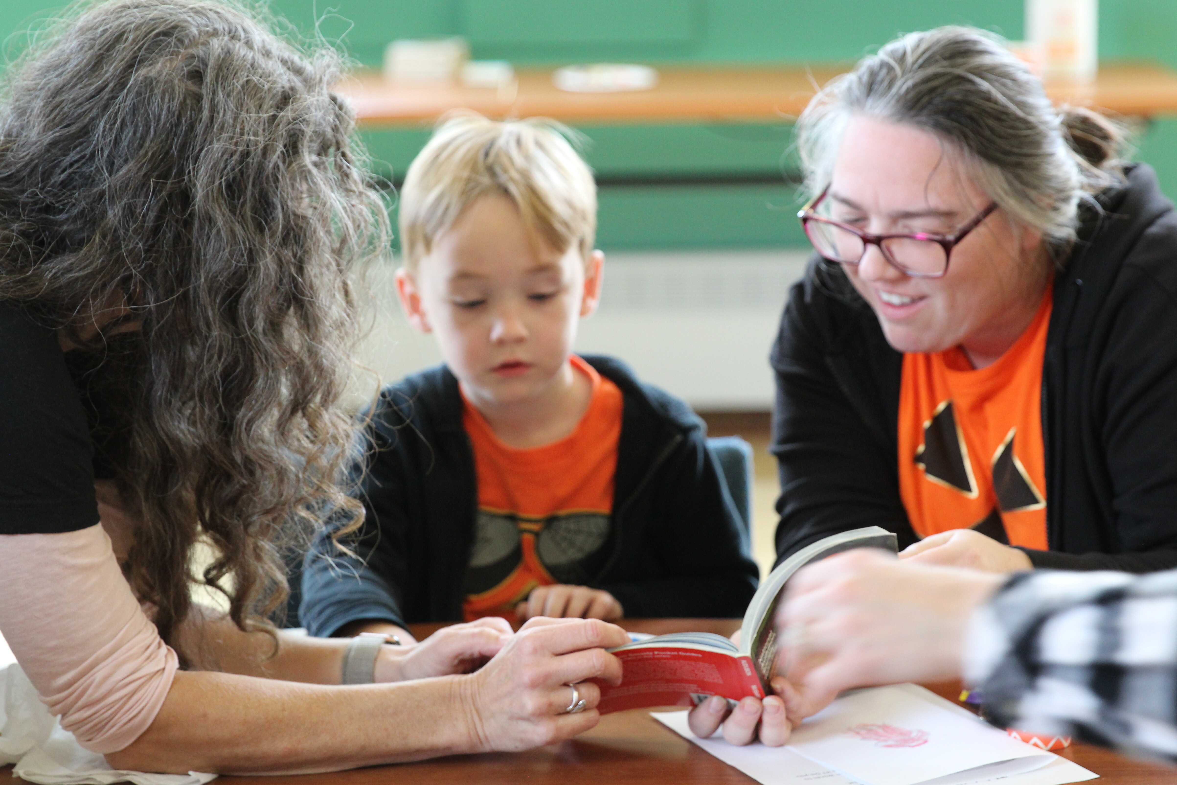 Two adults and a child sharing a book at a table, engaged in a thoughtful discussion.