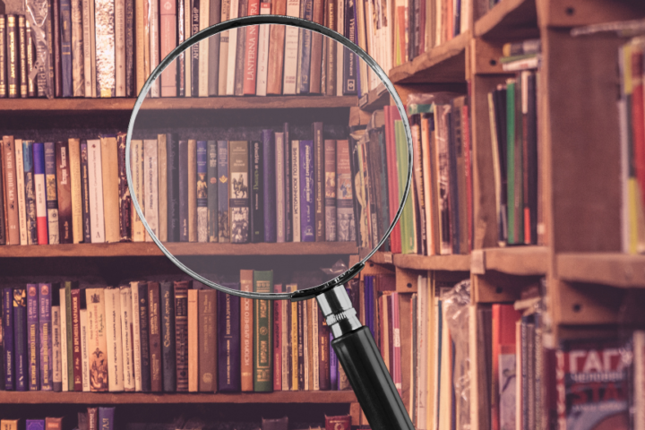 Magnifying glass focusing on books on library shelves representing research and information search