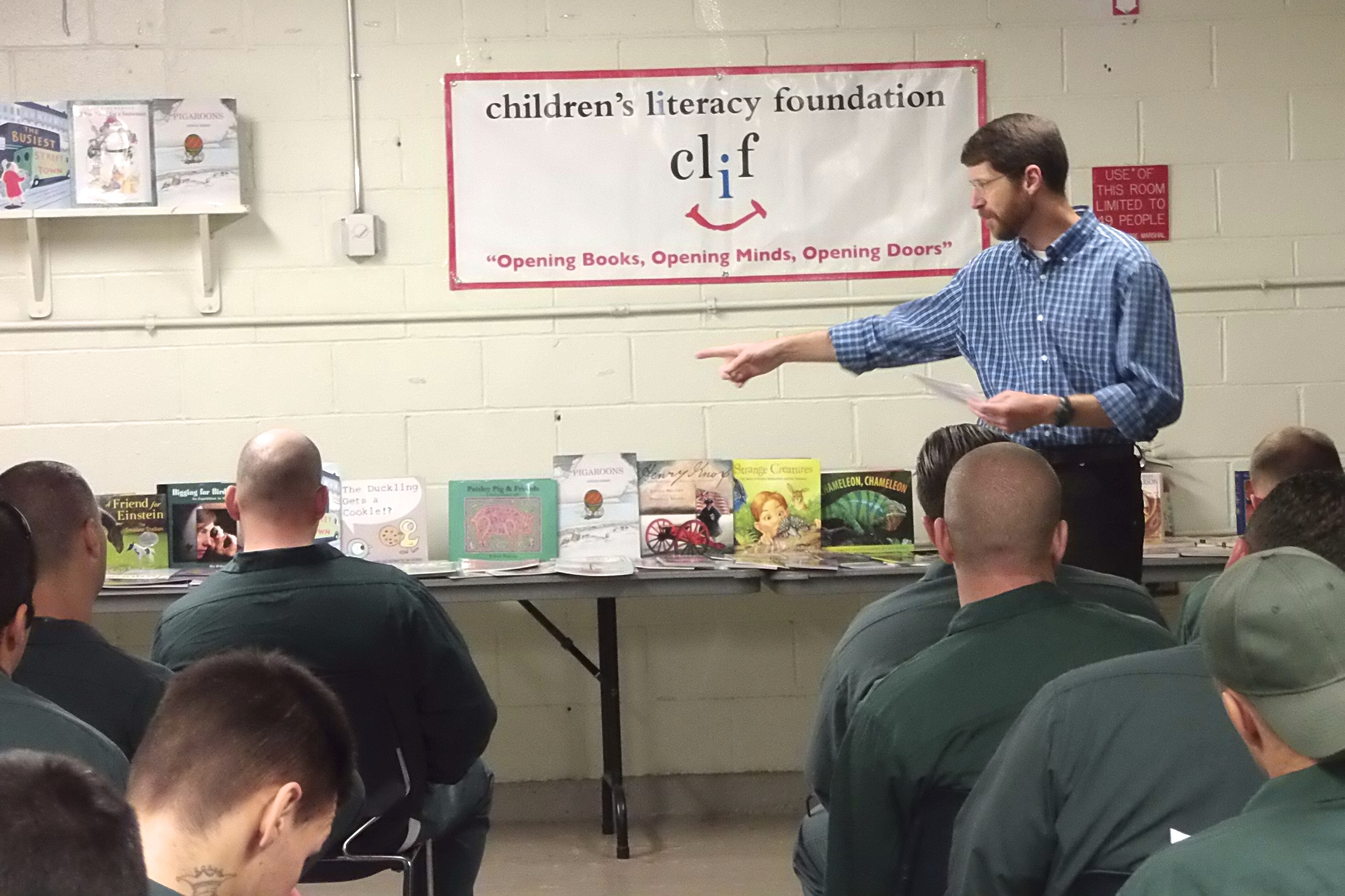 A speaker engages an audience in front of children&rsquo;s books, promoting literacy.