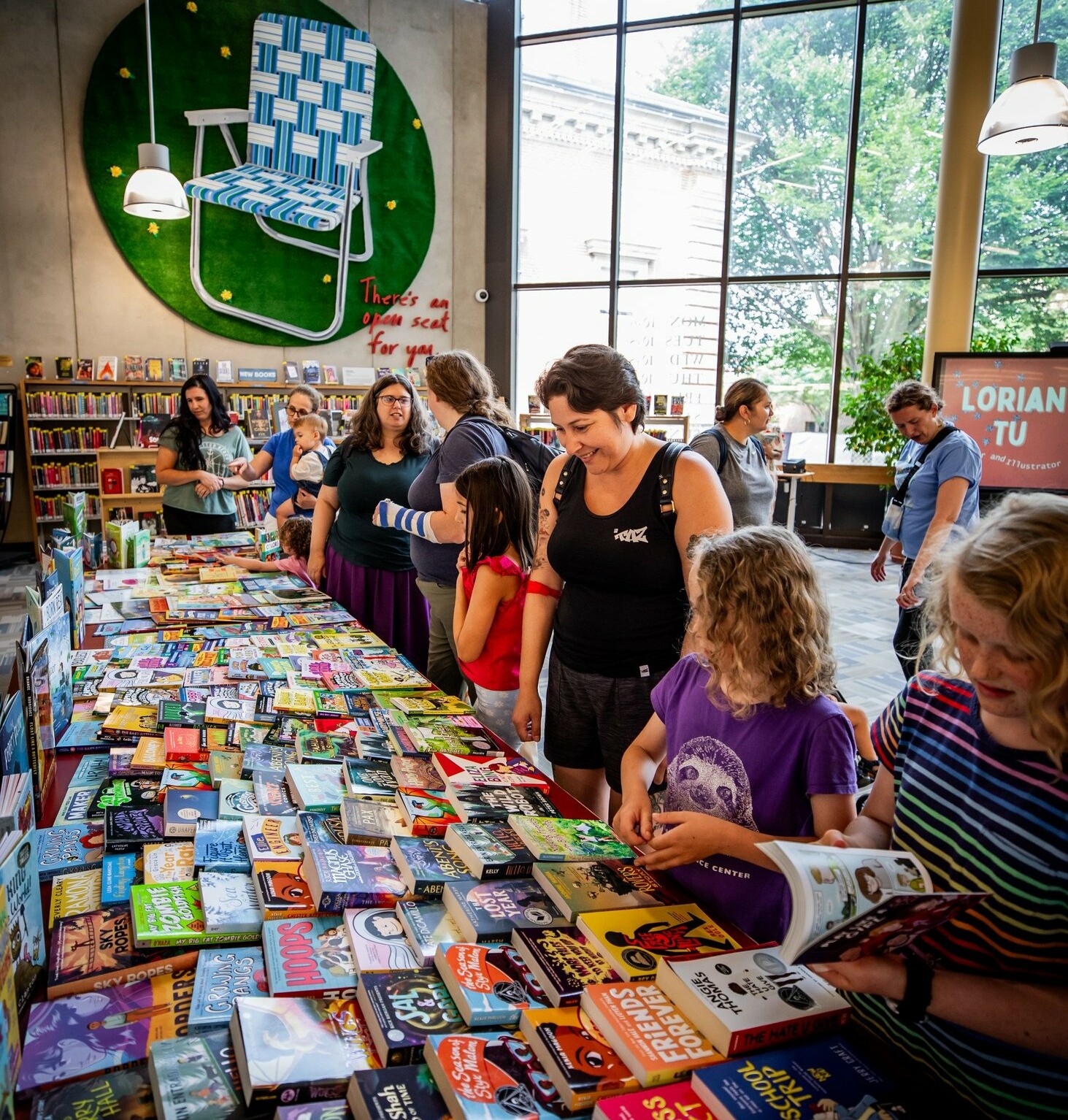 People browsing a table filled with colorful books in a modern library setting.