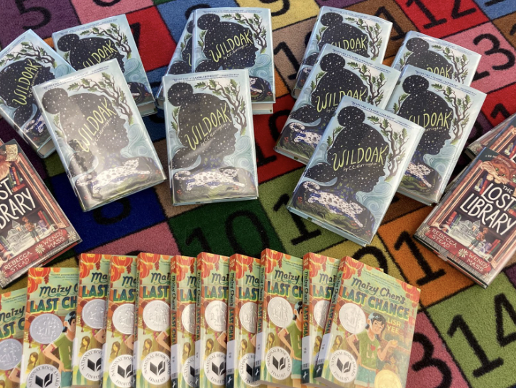 Multiple copies of "Wildoak," "Maizy Chen's Last Chance," and "The Lost Library" on a colorful rug.