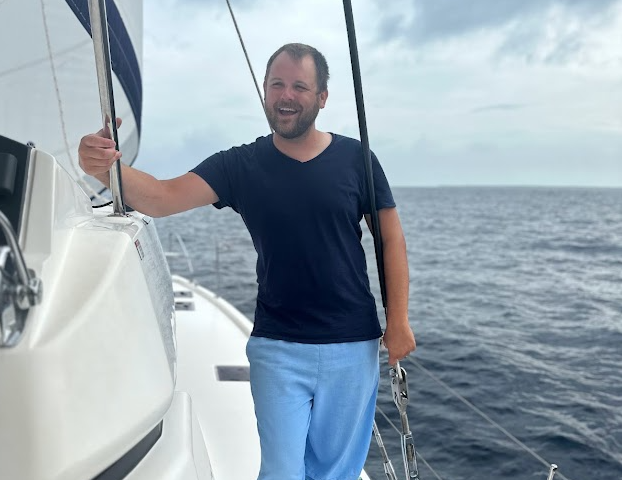 Trevor Luce, CLiF volunteer, standing on a sailboat deck with the open ocean in the background.