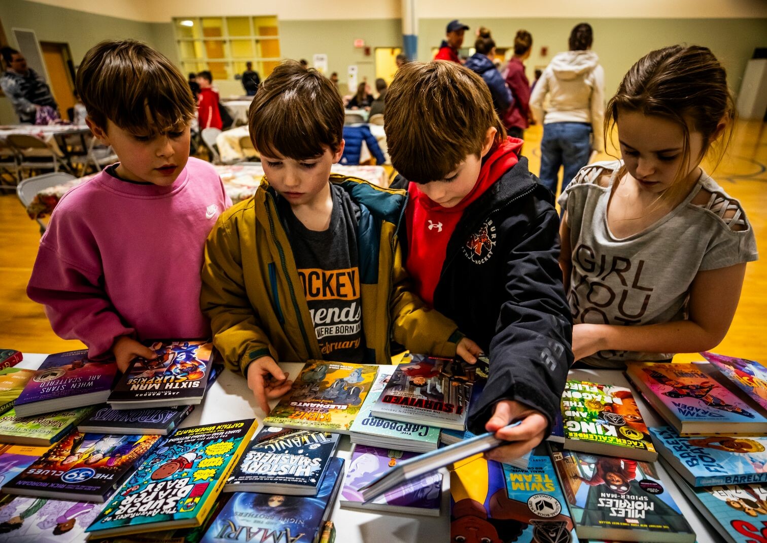 Four children gather around a table, inspecting a variety of colorful books.