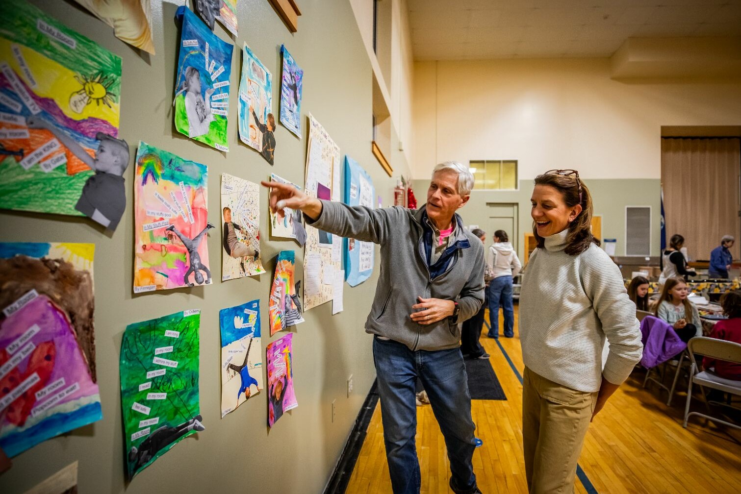 Two people discuss artwork displayed on a wall in a community center.