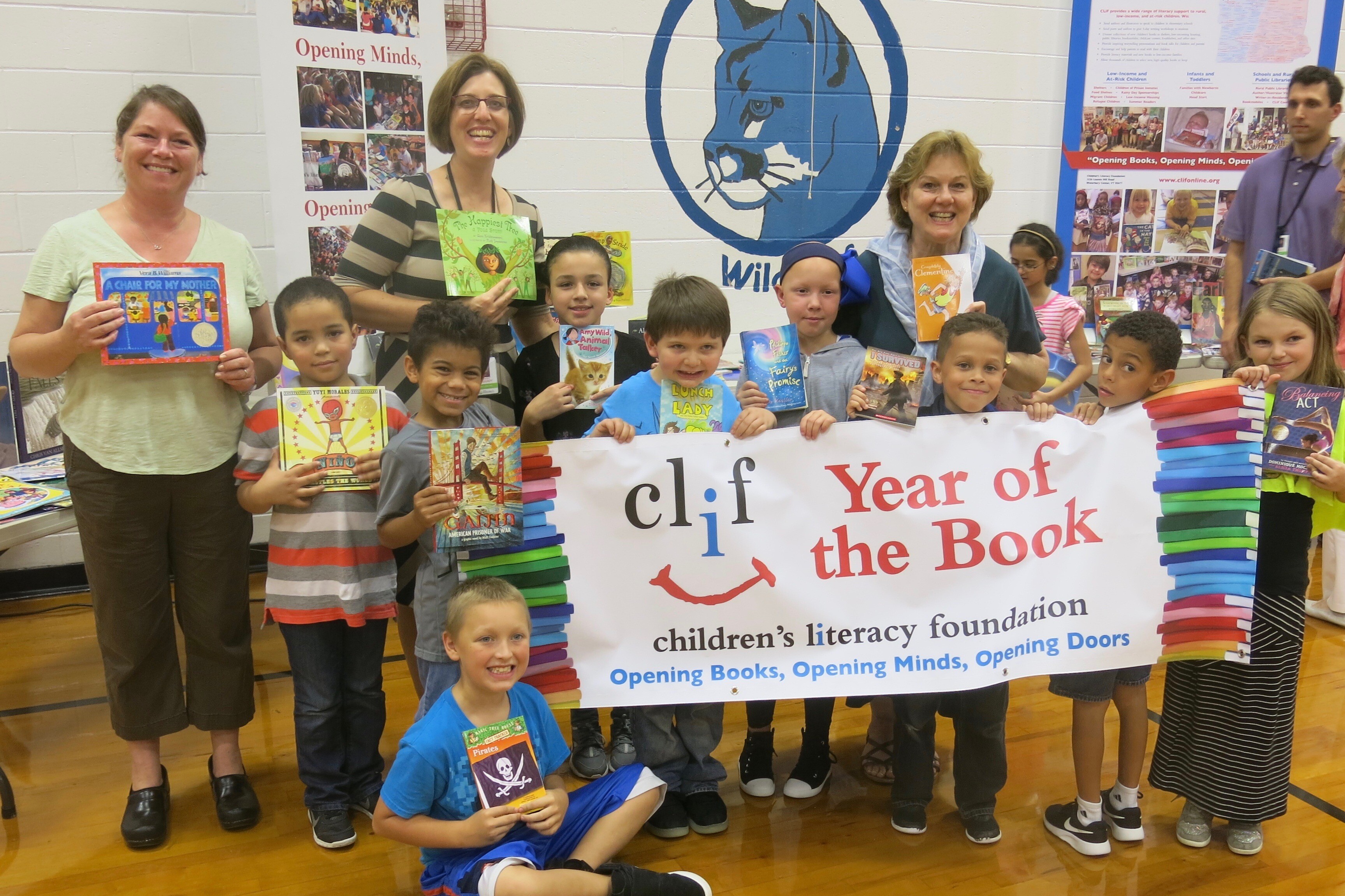 Group of children and adults holding books at a literacy event with a "Year of the Book" banner.