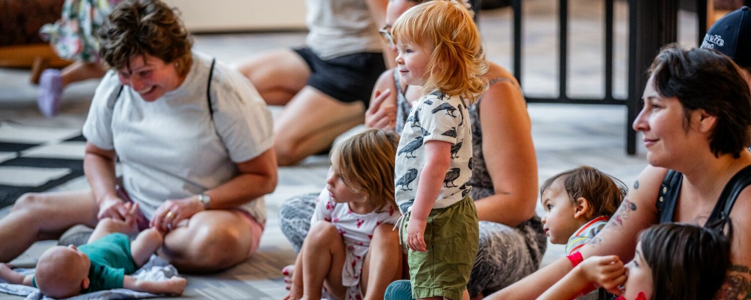 A group of children and adults engaged in an activity on the floor of a bright room.
