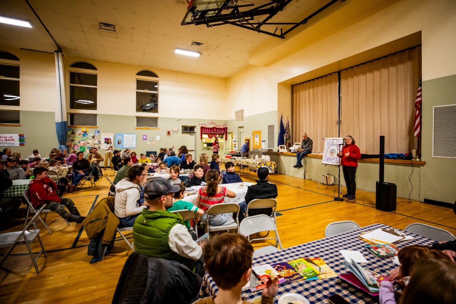 Community event in a hall with attendees seated, listening to a speaker at a podium.