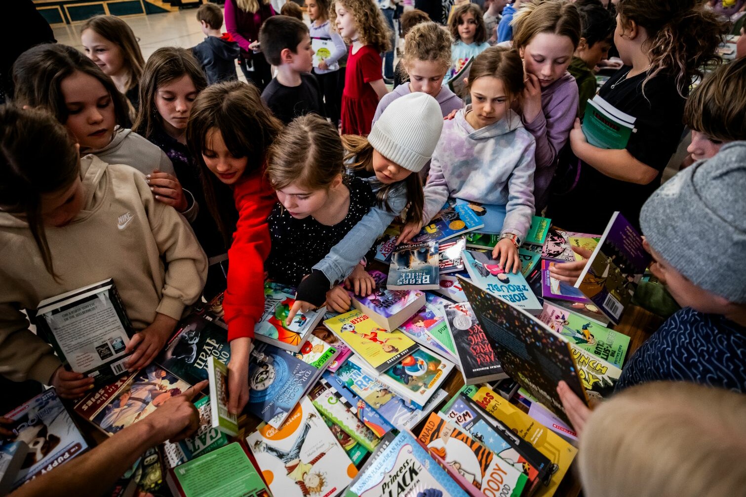 Children eagerly explore a large collection of books at a busy table.