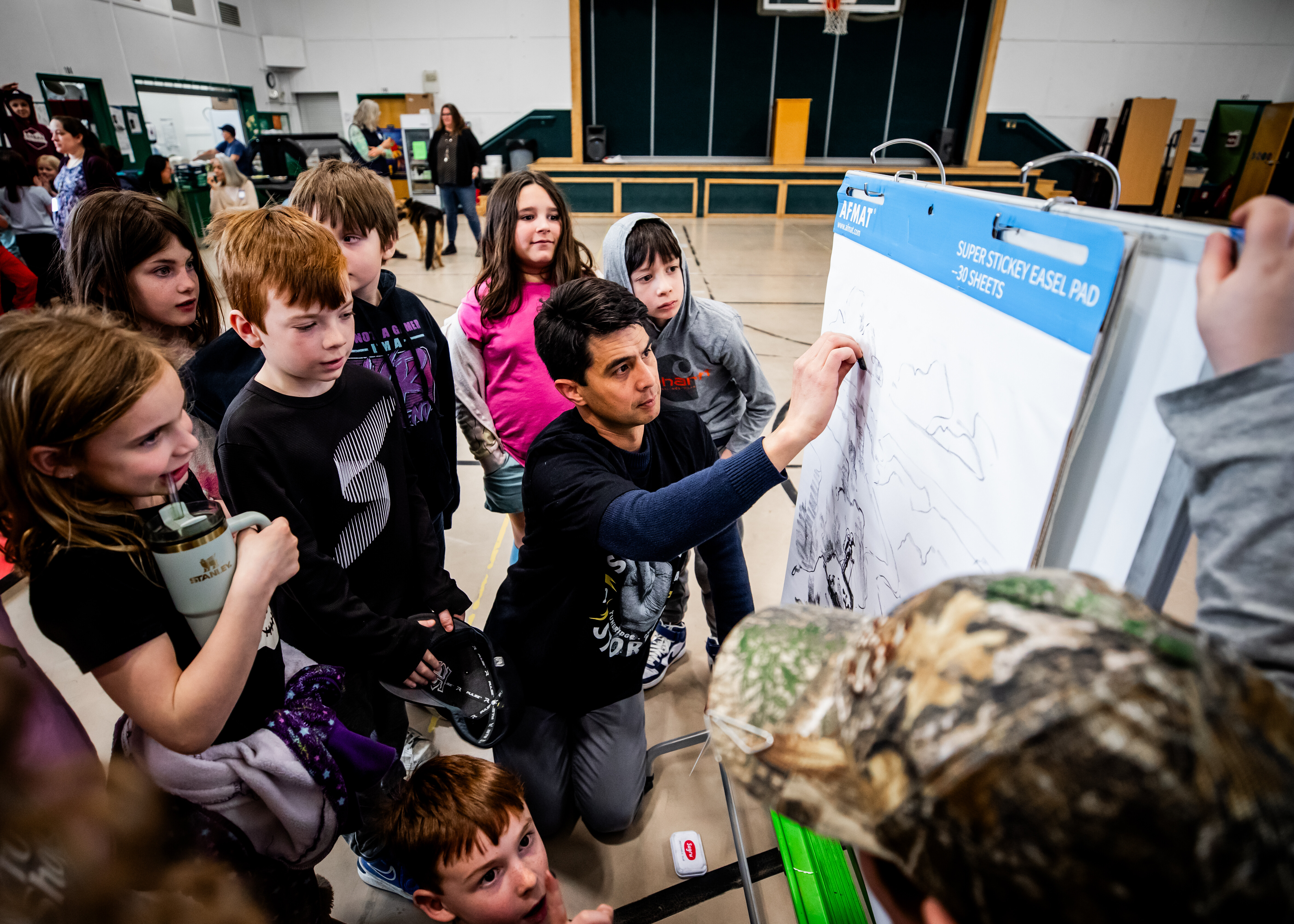 An educator draws on an easel while a group of engaged children watch closely.