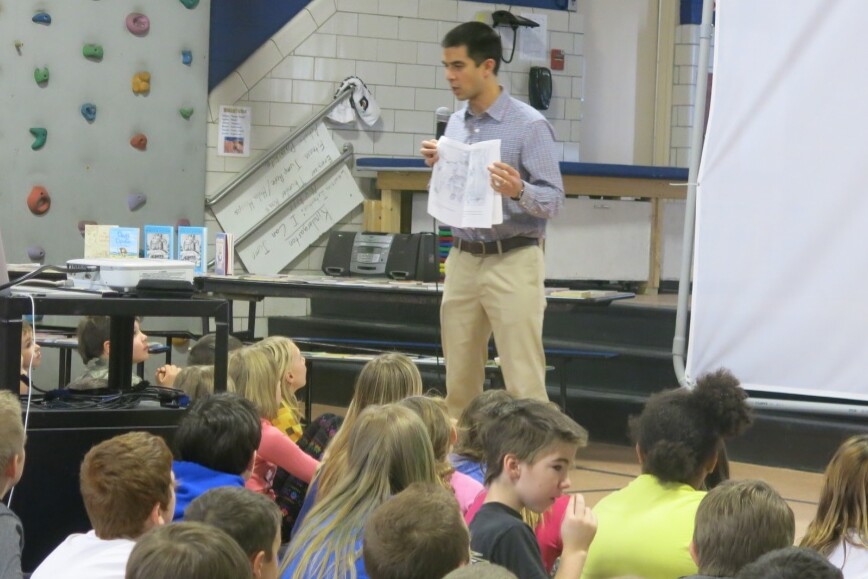 Teacher speaking to a group of elementary students during a school assembly presentation