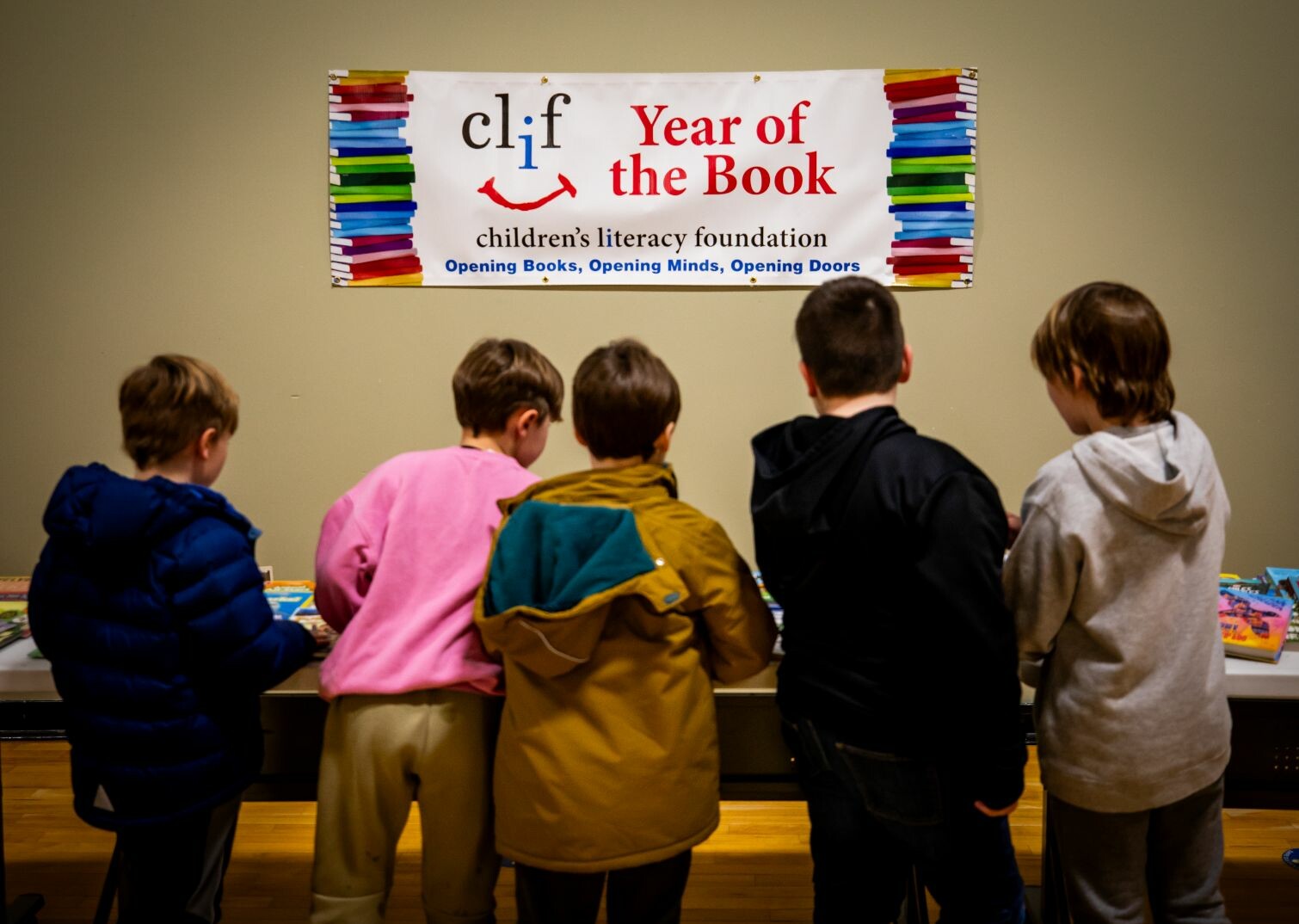Children gather around a table, exploring books under a literacy program banner.
