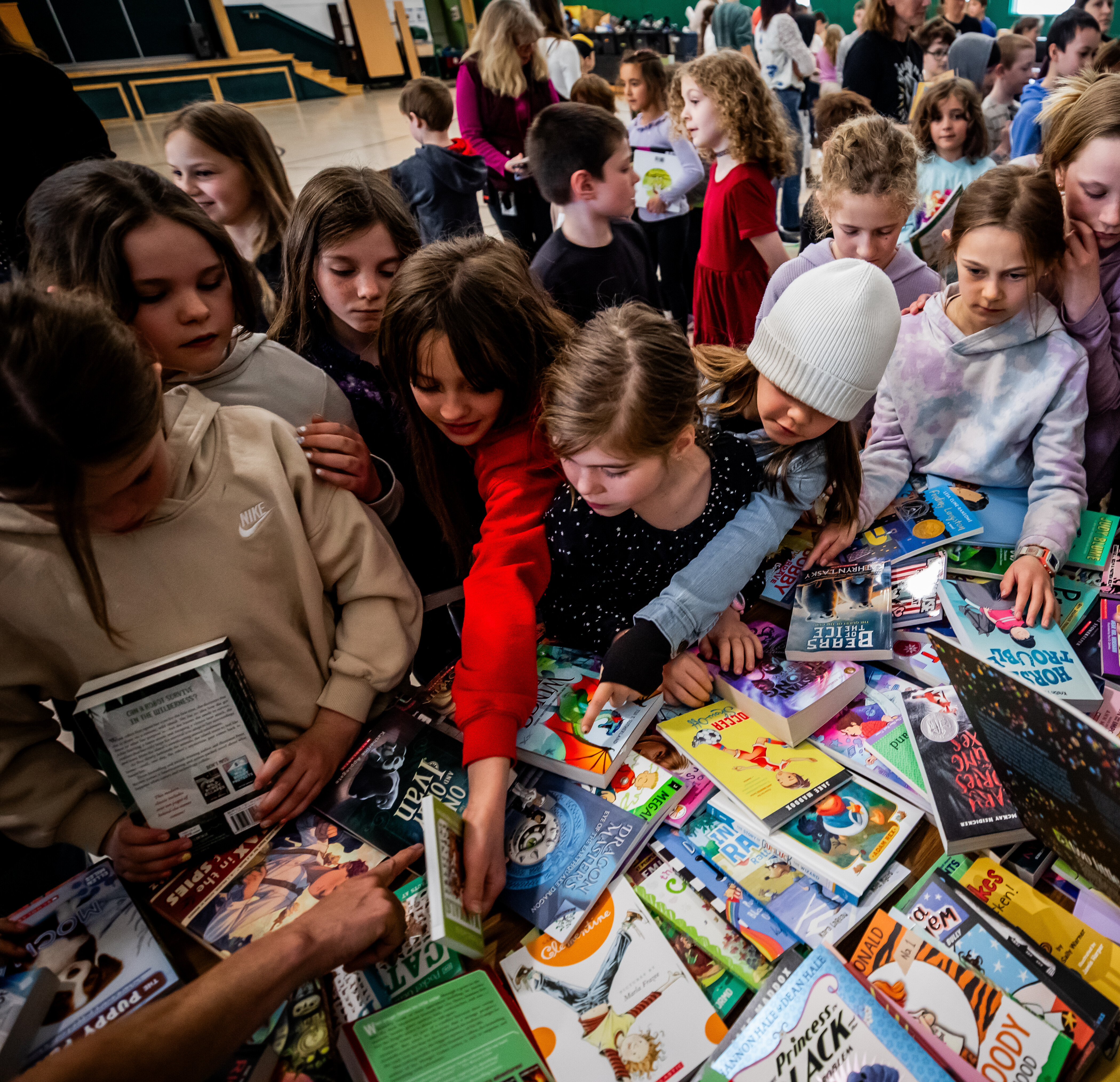 Children eagerly selecting books from a colorful table piled with various titles.