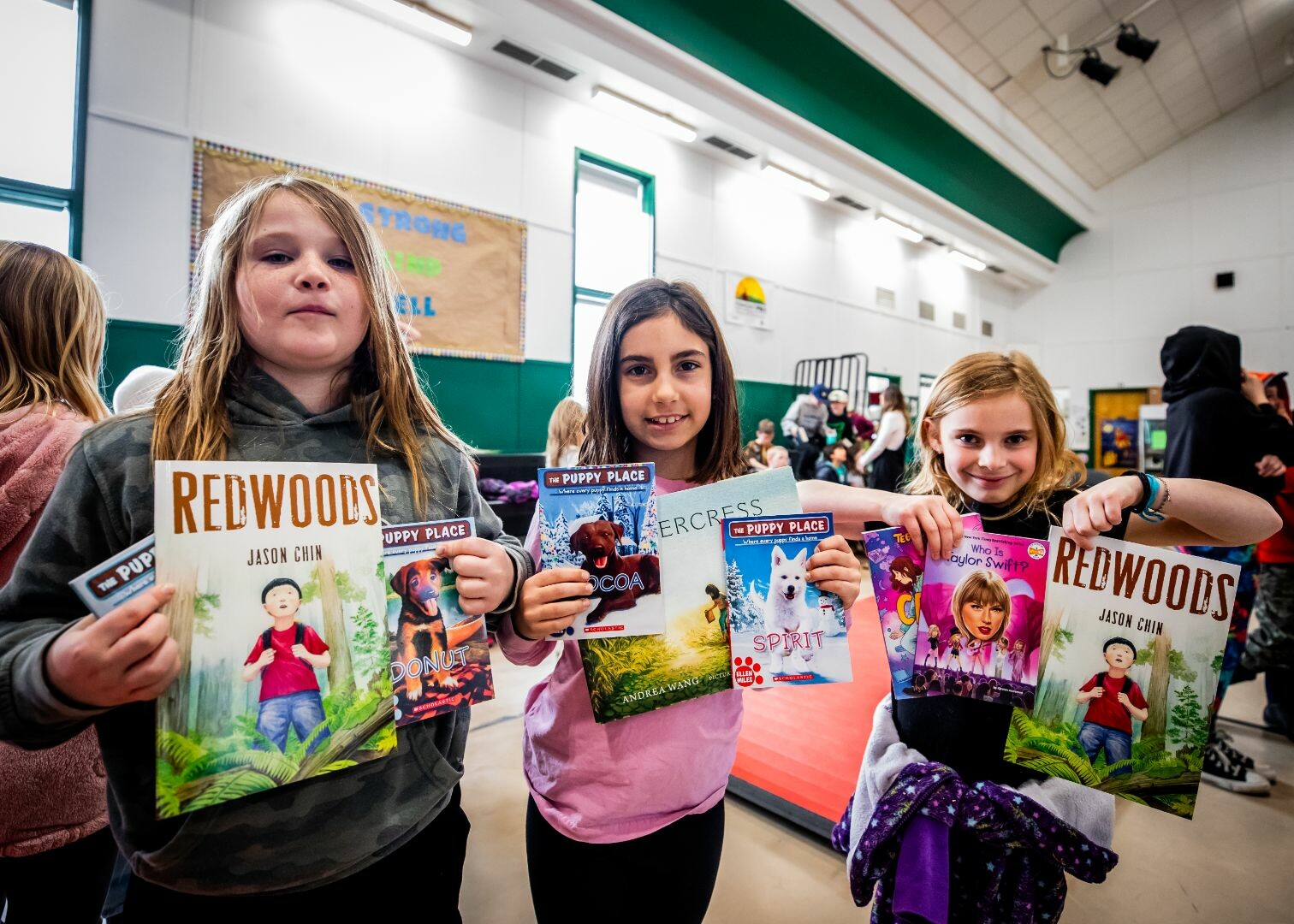 Three children hold books titled "Redwoods" and various "Puppy Place" titles, smiling.