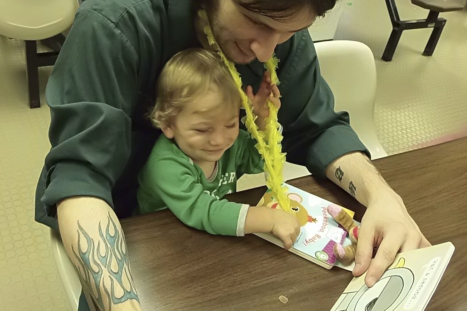 A smiling child and caregiver share a colorful book, engaging in playful reading together.