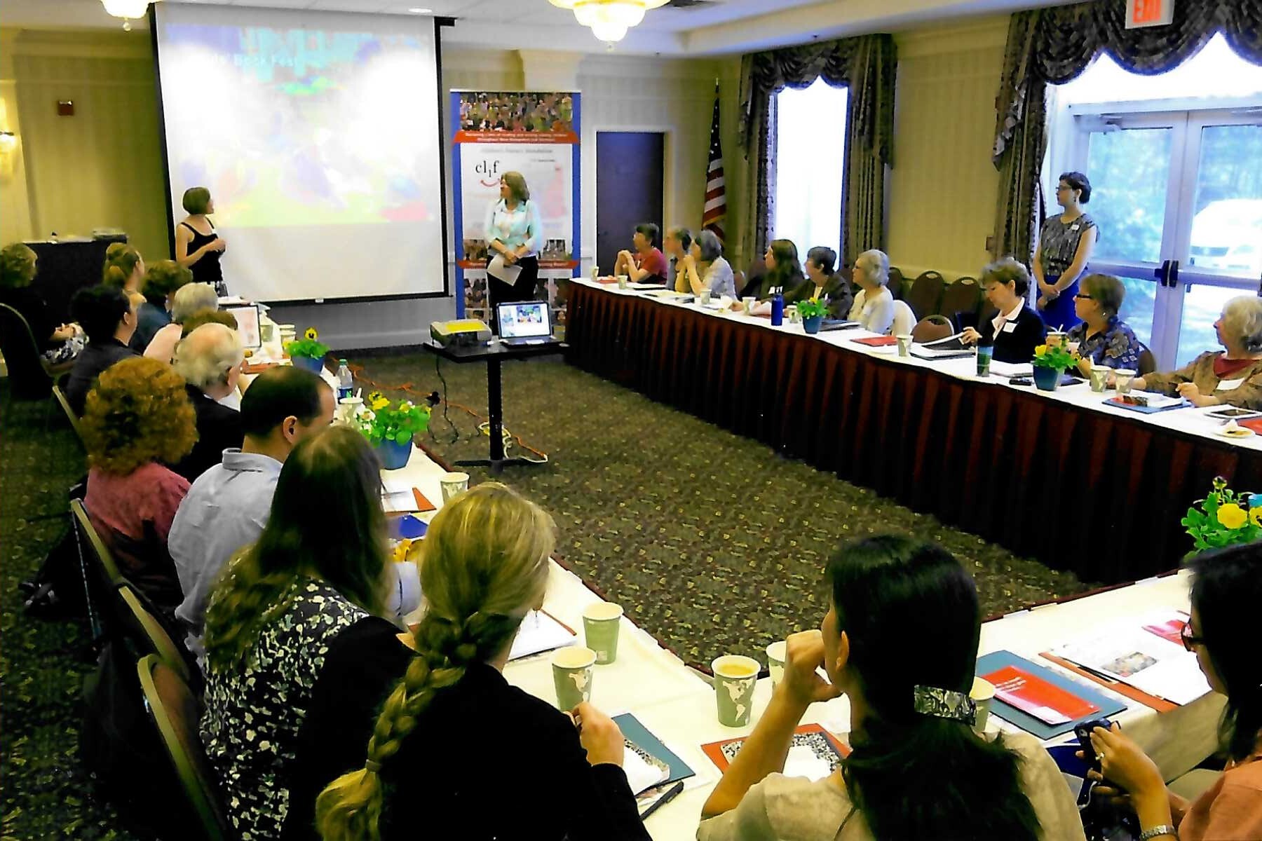 Group of people seated at a table in a conference room, listening to a presentation.