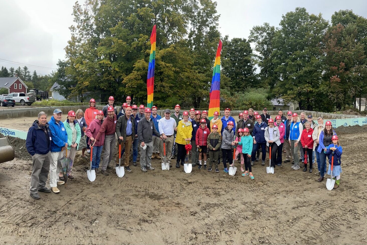Group photo at a groundbreaking ceremony with colorful flags and hard hats.