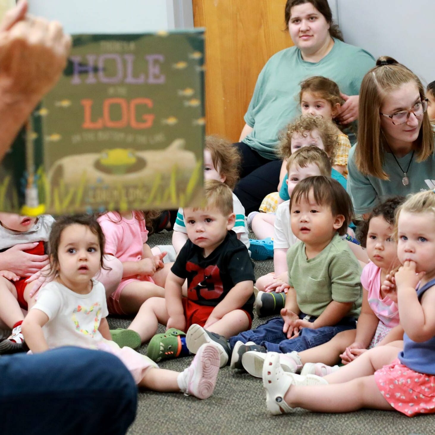 A group of toddlers attentively listens to a story being read to them.