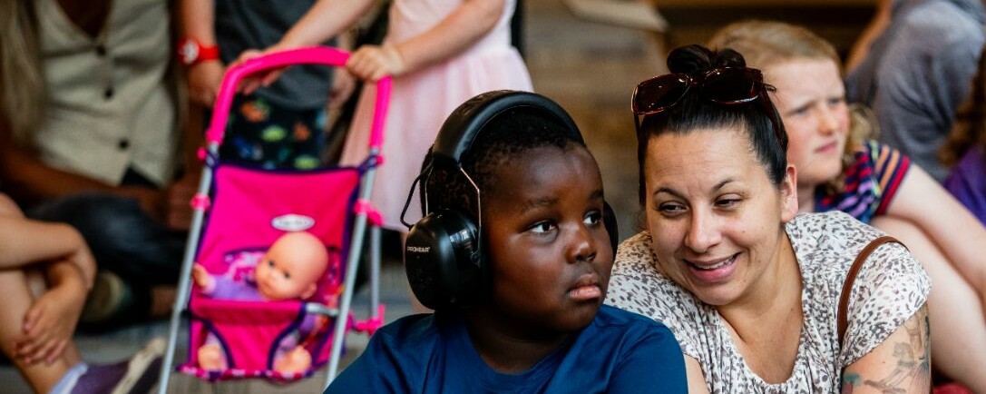 A boy with headphones sits beside a woman, both looking attentively at something off-camera.