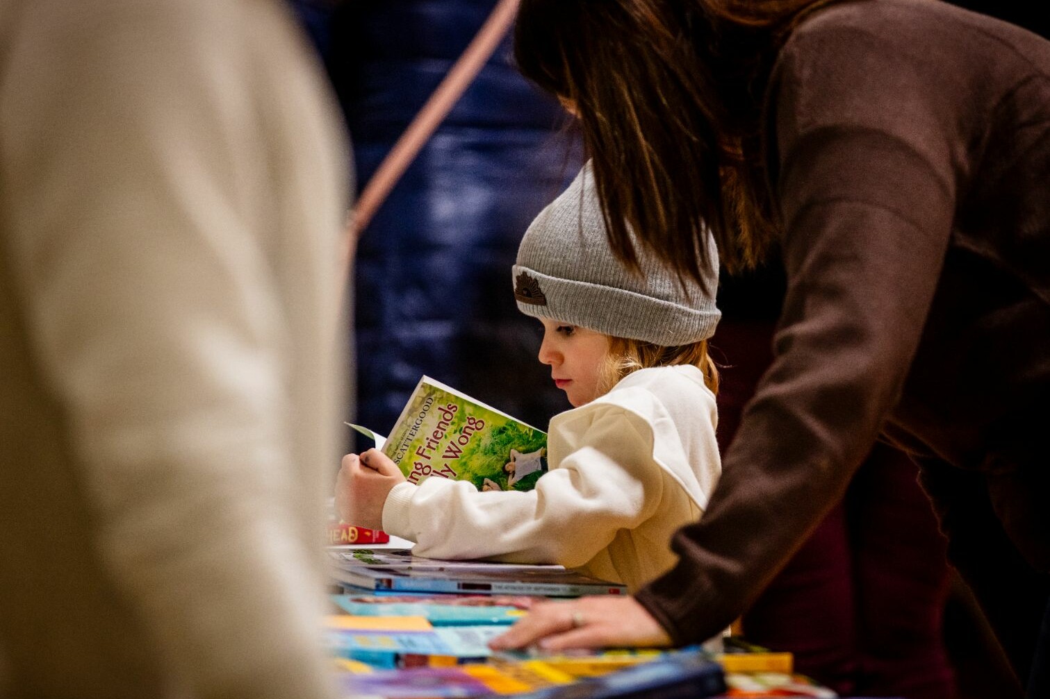 Child reading a book at a table filled with colorful children's books.