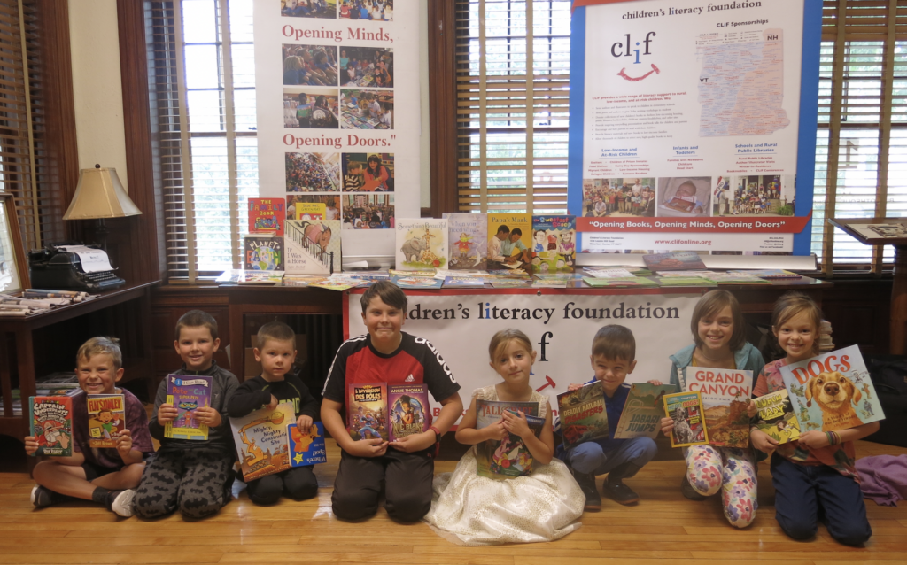 Students proudly displaying new books at a CLiF children&rsquo;s literacy program with book displays behind them.