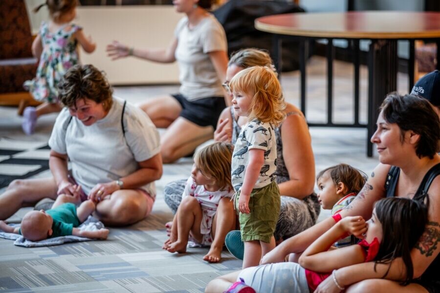 Parents and toddlers interacting on a carpeted floor in a casual group setting.