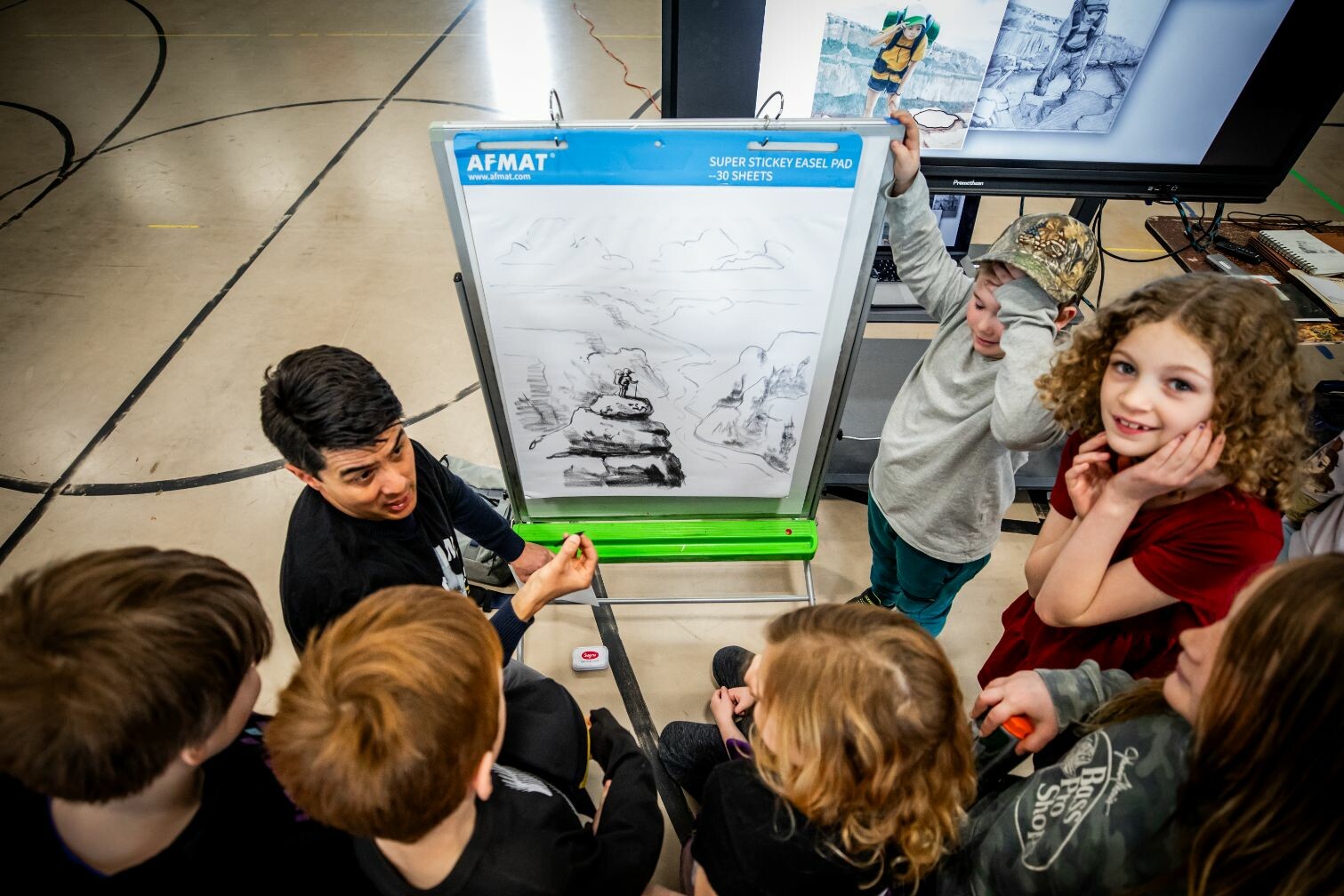 An instructor engages a group of attentive children during an art demonstration.