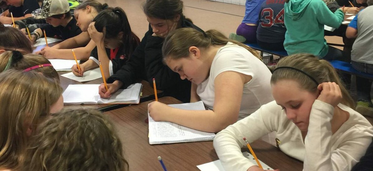 Students focused on writing in notebooks at a classroom table.