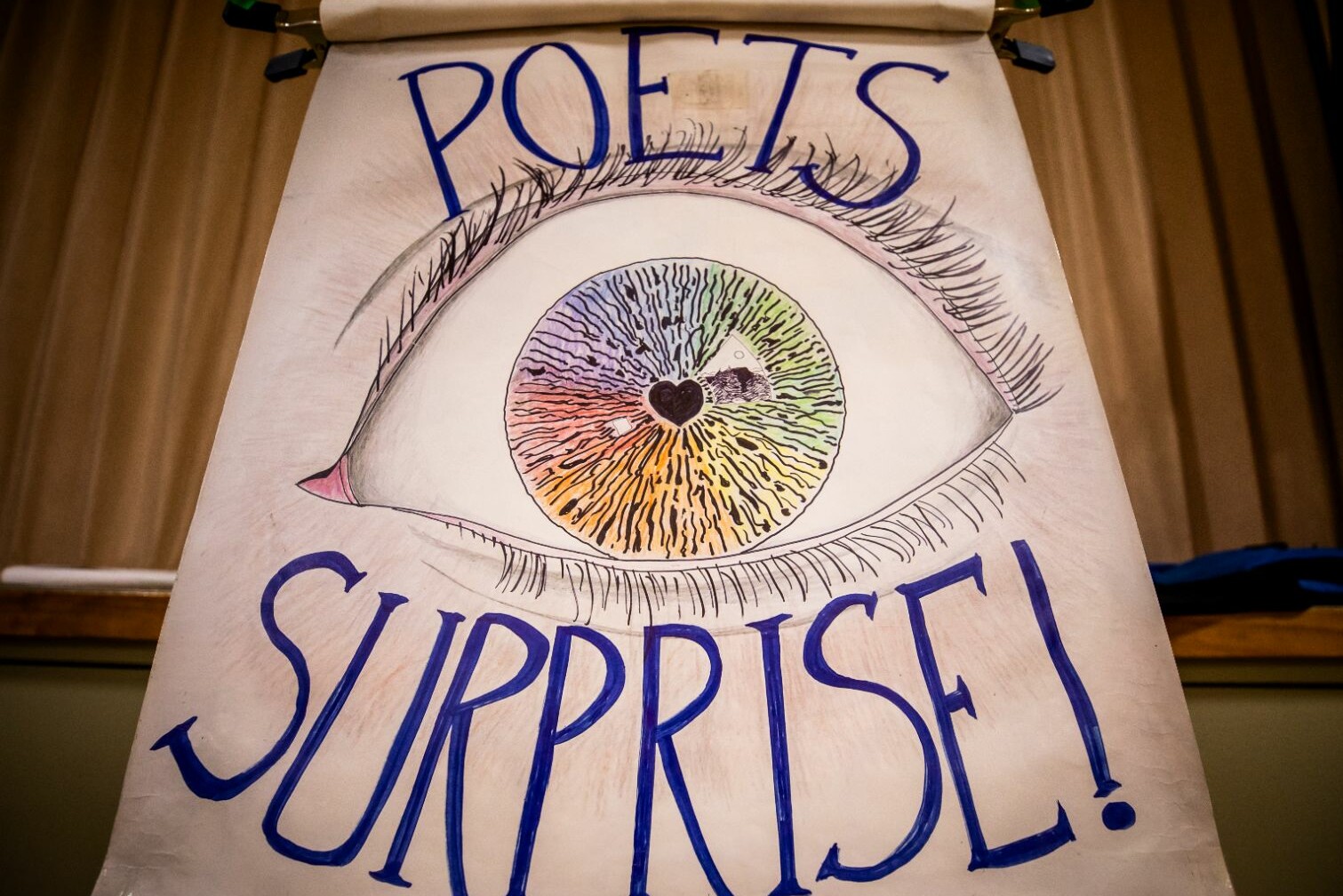 A colorful eye illustration with the words "POETS SURPRISE!" beneath it.