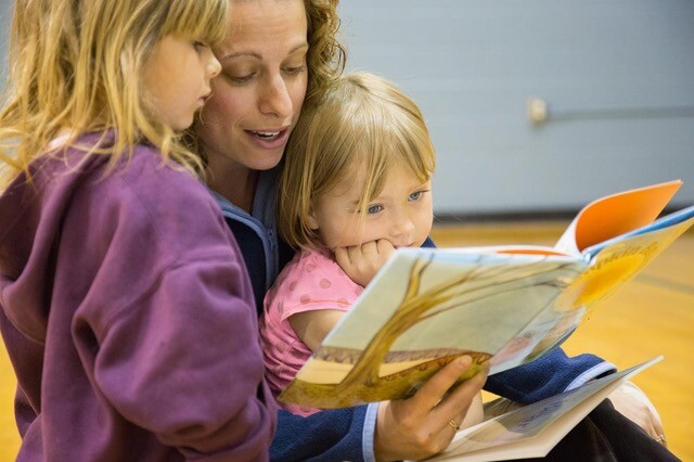Mother reading a picture book with two young children sitting together indoors