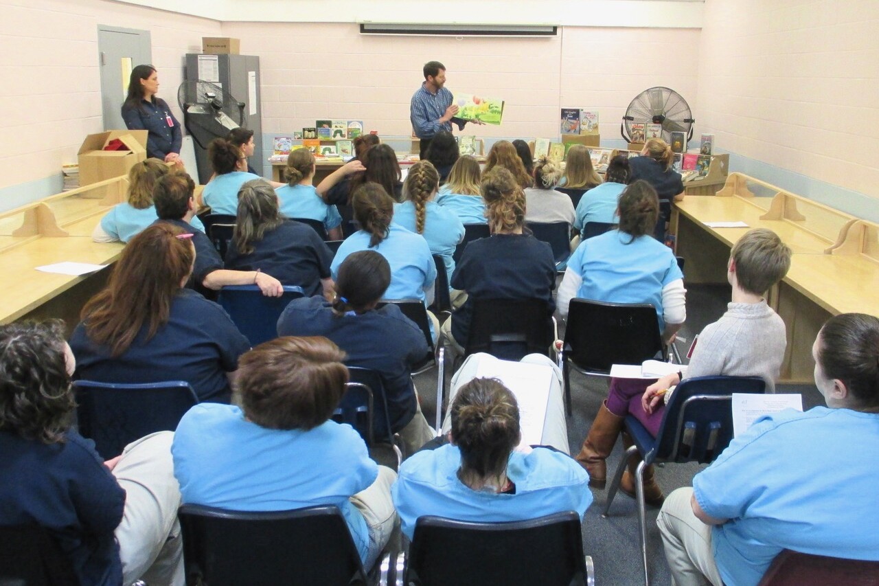 A speaker presents to an audience of women, seated and listening attentively.
