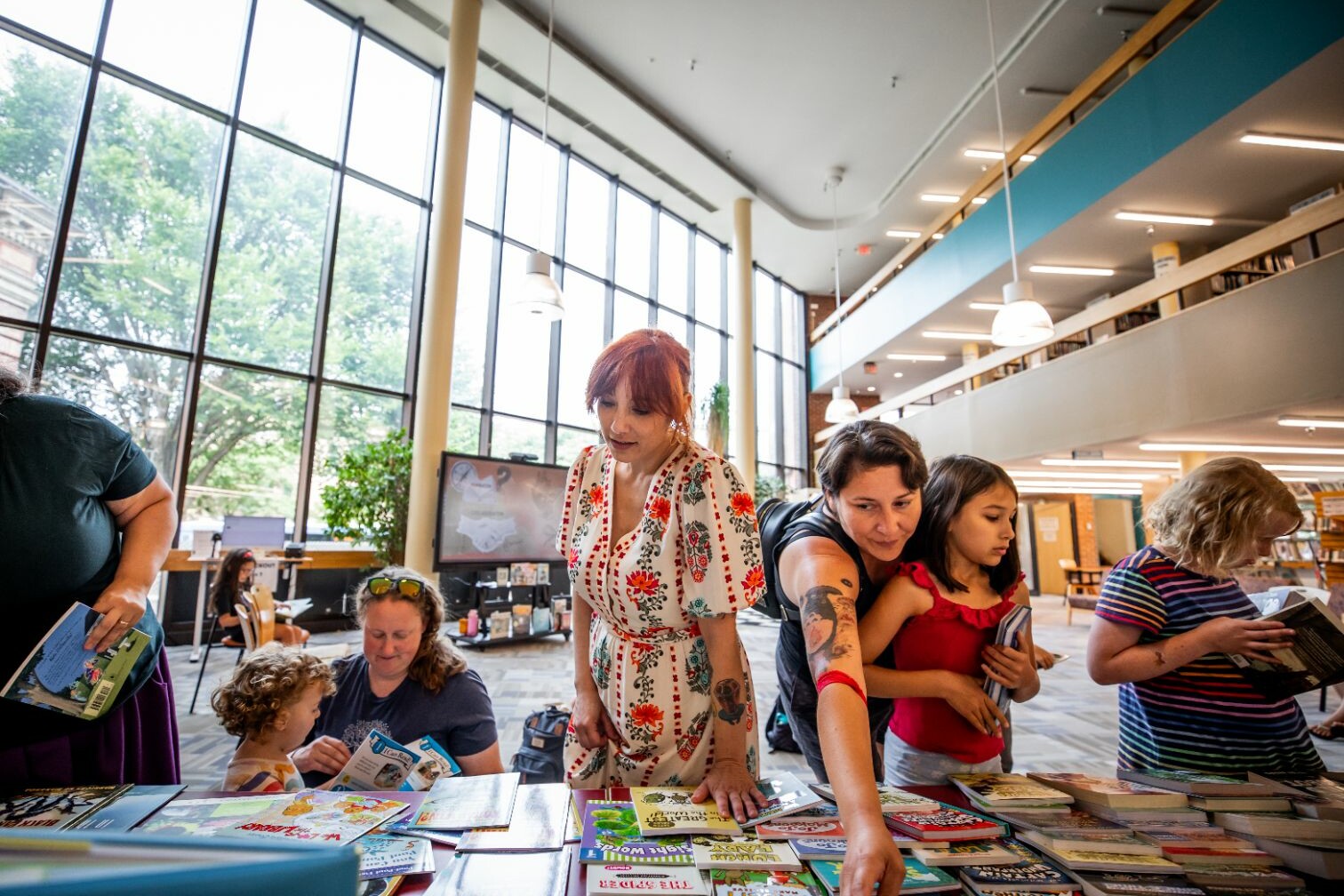 People browsing books at a library, with large windows in the background.