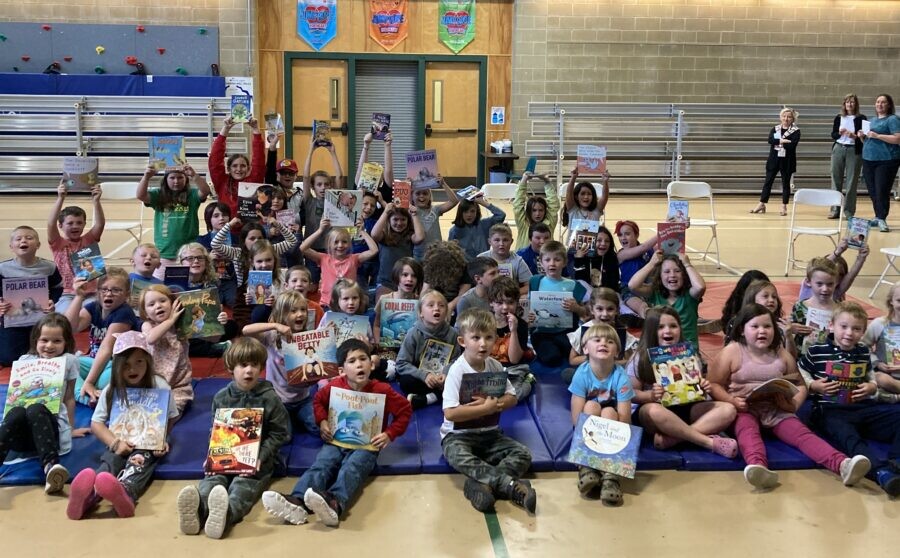 Students sitting together in a gym holding books received during a school literacy celebration.
