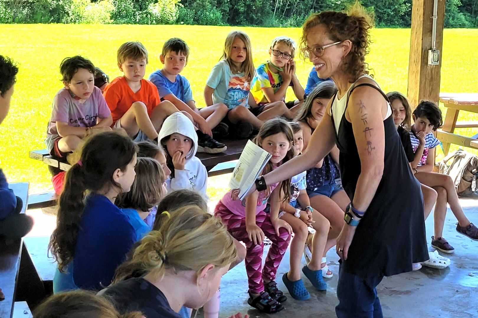 A teacher engages with attentive children in an outdoor classroom setting.