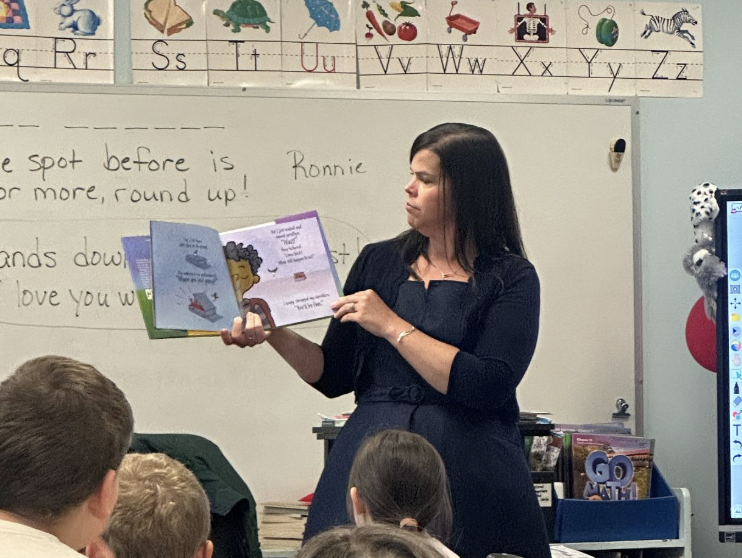Teacher reading a book to students in a classroom setting.