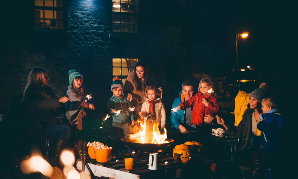 Families and children gathered around a backyard fire pit holding sparklers at night.
