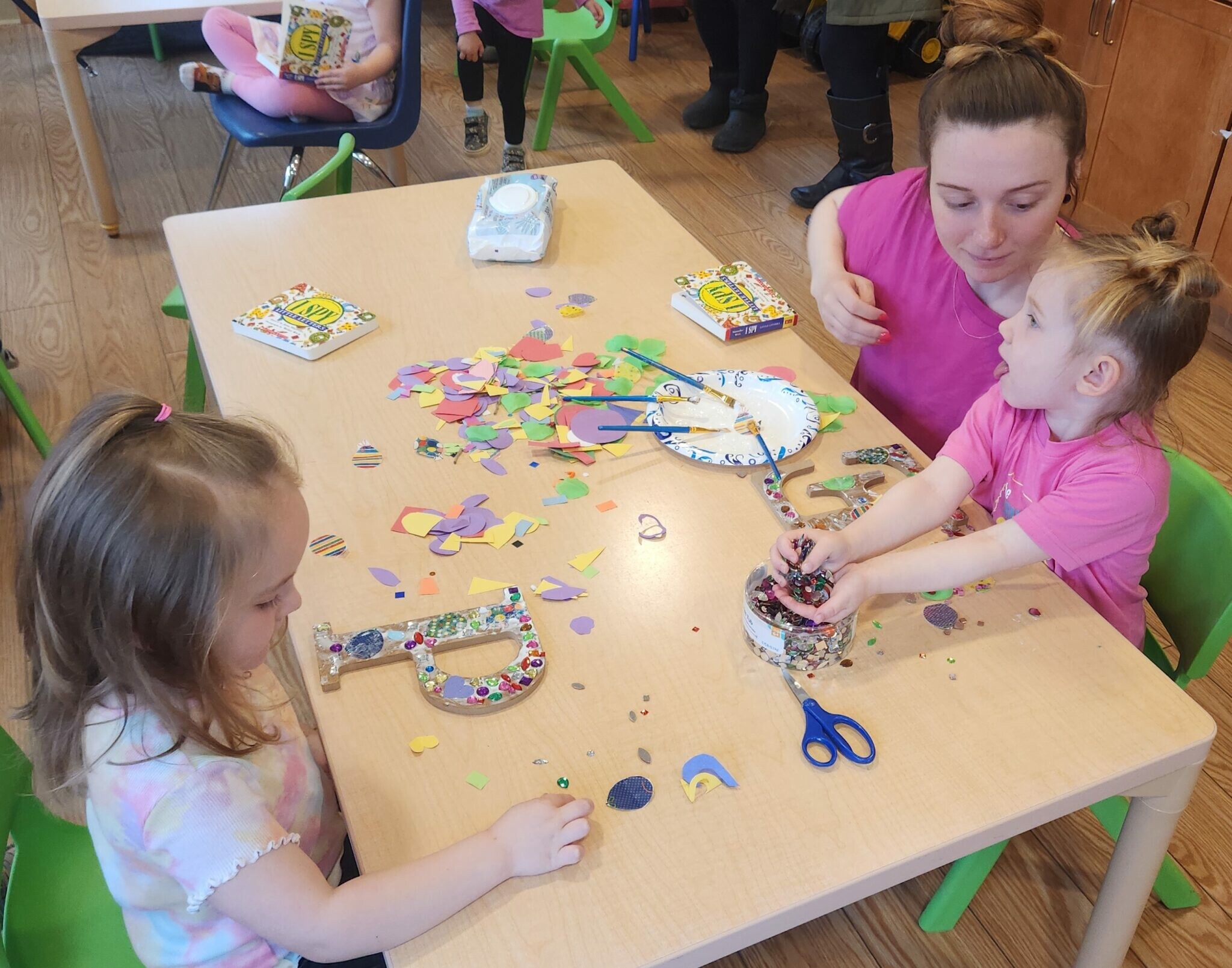 Kids and an adult create art with colorful paper shapes at a table.