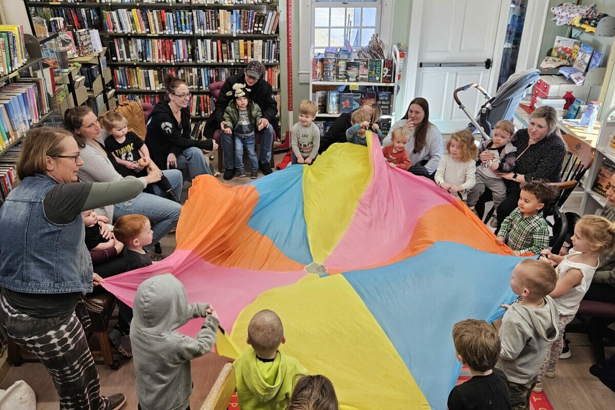 Children and adults play with a colorful parachute in a library setting.