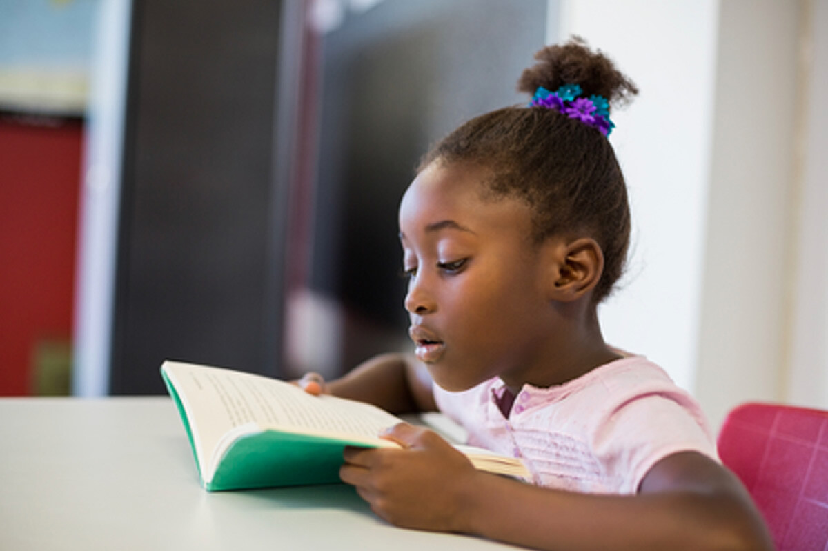 A girl reading a book intently at a table, focused on the page.
