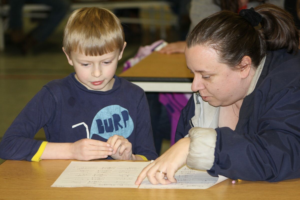 A child and adult review a paper while engaged in discussion at a table.