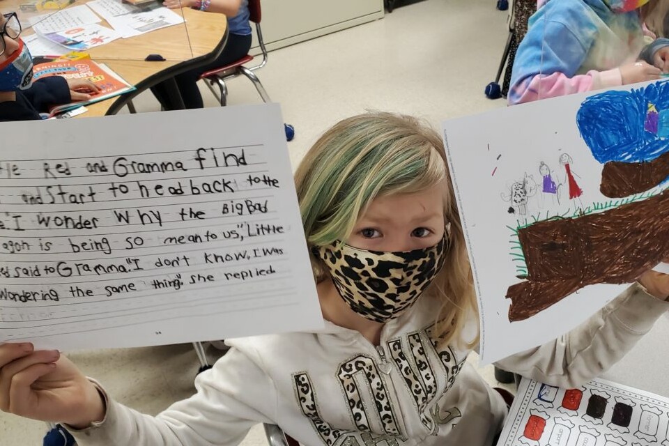 Child displaying school assignment with writing and illustration during a classroom literacy activity