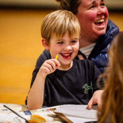 Smiling boy holding a pencil and laughing during a group learning activity.