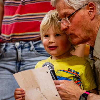 Older man leaning close to a young child as they look at a book together.