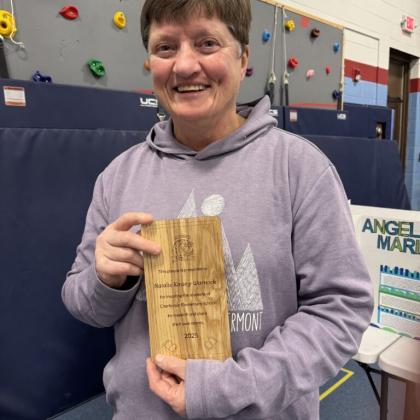 Adult holding a wrapped book and smiling at a school or community event.